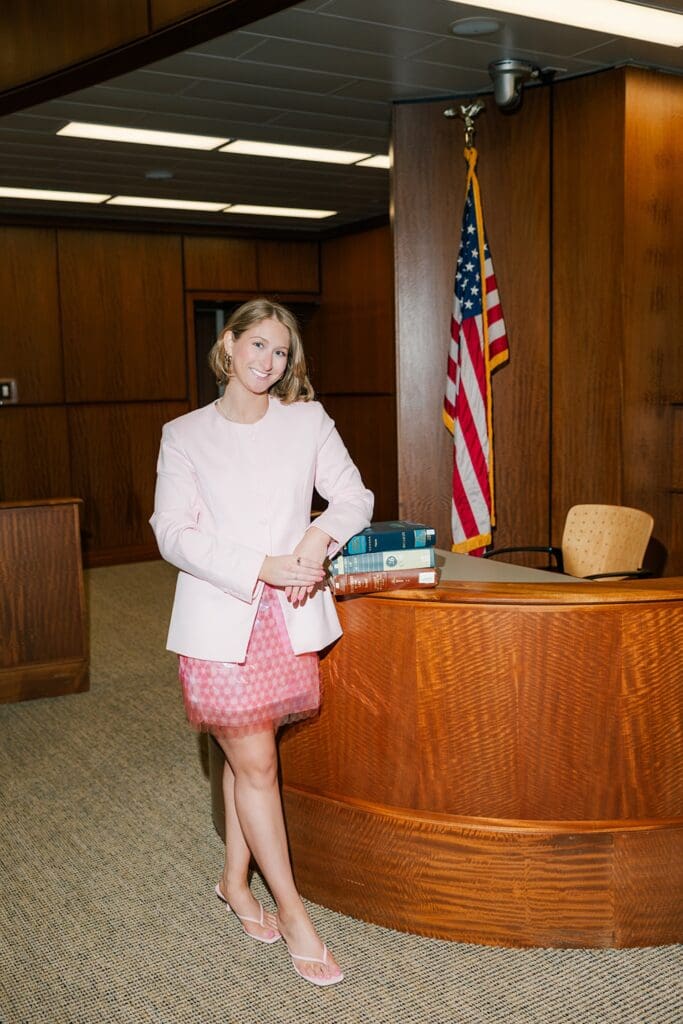Abby smiles and stands with books in the courtroom at QU Law school. 