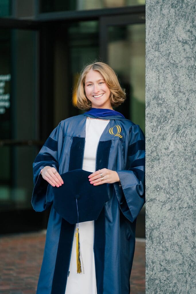 Abby holds her cap and wears her gown. 