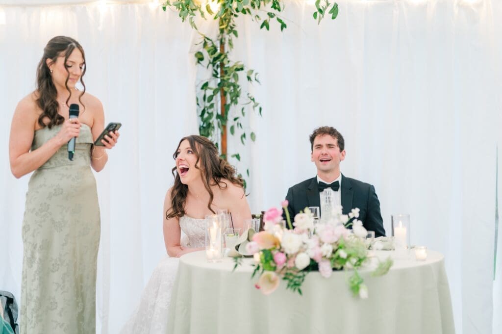 Miranda laughs as her sister gives a speech at their tented wedding reception. 