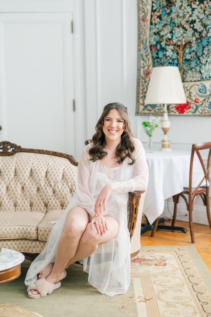 Miranda, the bride, sitting on a couch in the oval room at Aldworth Manor for her wedding in her bridal getting ready outfit. 