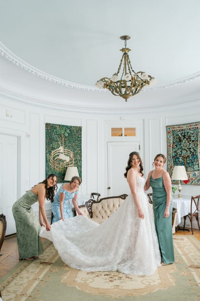 The bride's sisters and mom adjusting her wedding train in the oval room at Aldworth Manor for her wedding. 