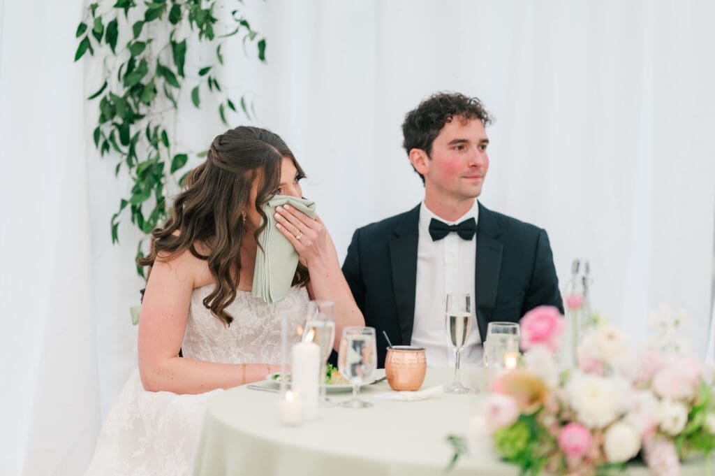 The bride dabs tears off her face during a speech. 