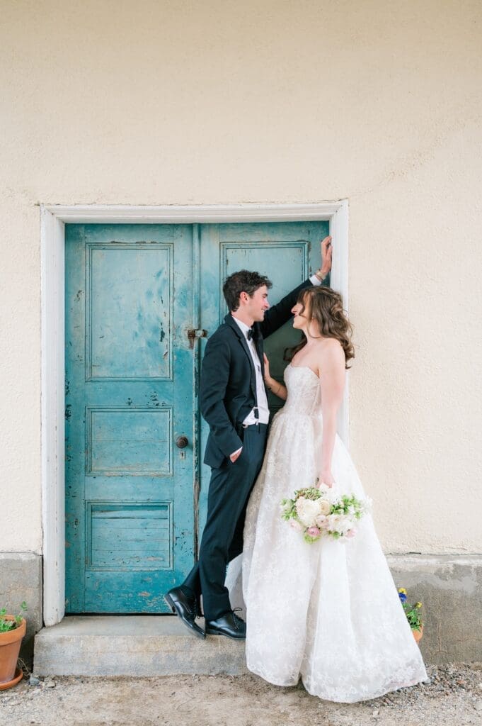 Mitch leans against Miranda next to a blue door. 