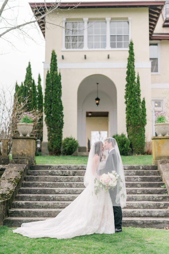 Miranda and Mitch kiss on the stairs outside of Aldworth Manor for a wedding portrait. 