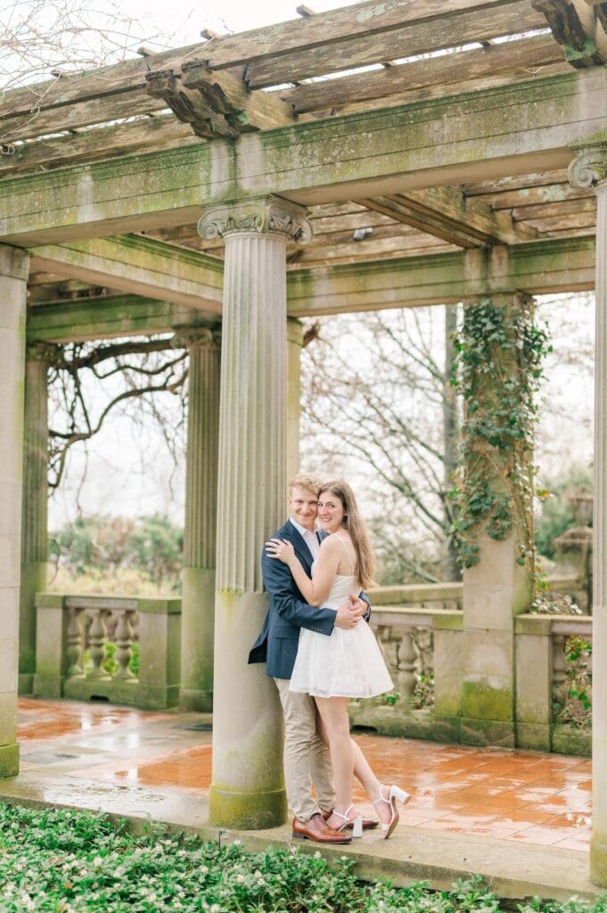 Dylan leans against a column and Sydney leans against him.