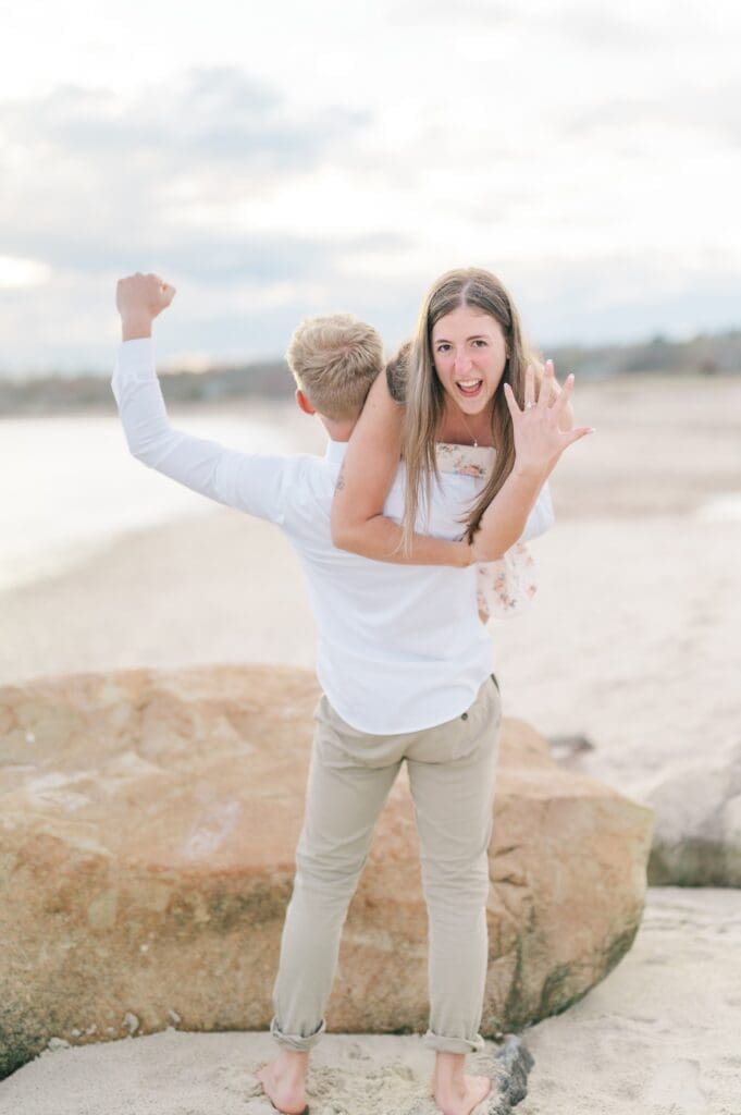 Dylan holds sydney on his shoulder and she holds up her hand with her ring while he cheers as he holds her. 