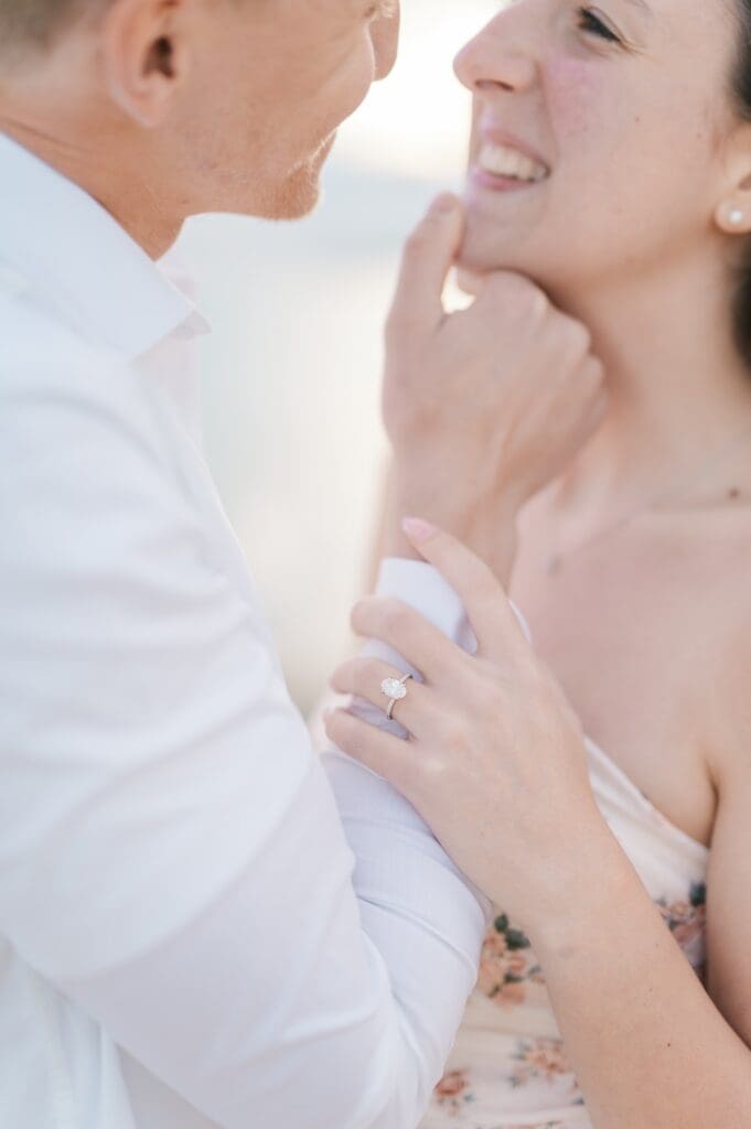 Dylan grabs Sydney's chin and brings it towards his face. Sydney's oval cut diamond ring is in the foreground. 