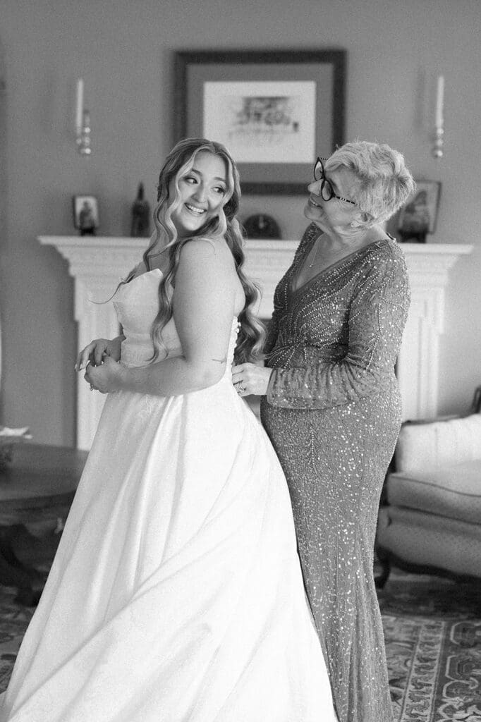 Magdalene's mom smiles at her as she buttons up her dress. 