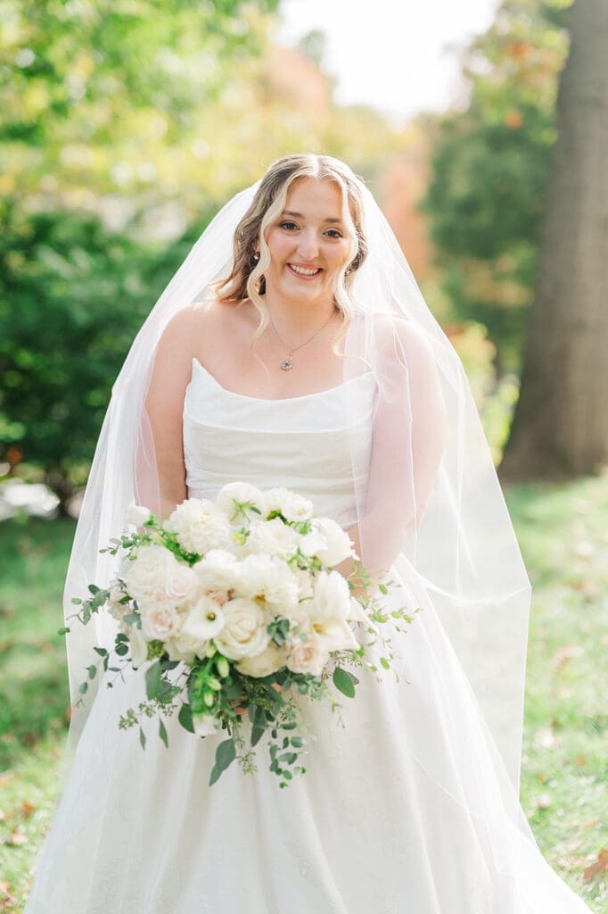 Magdalene smiles as she holds a bouquet of white florals with greenery 