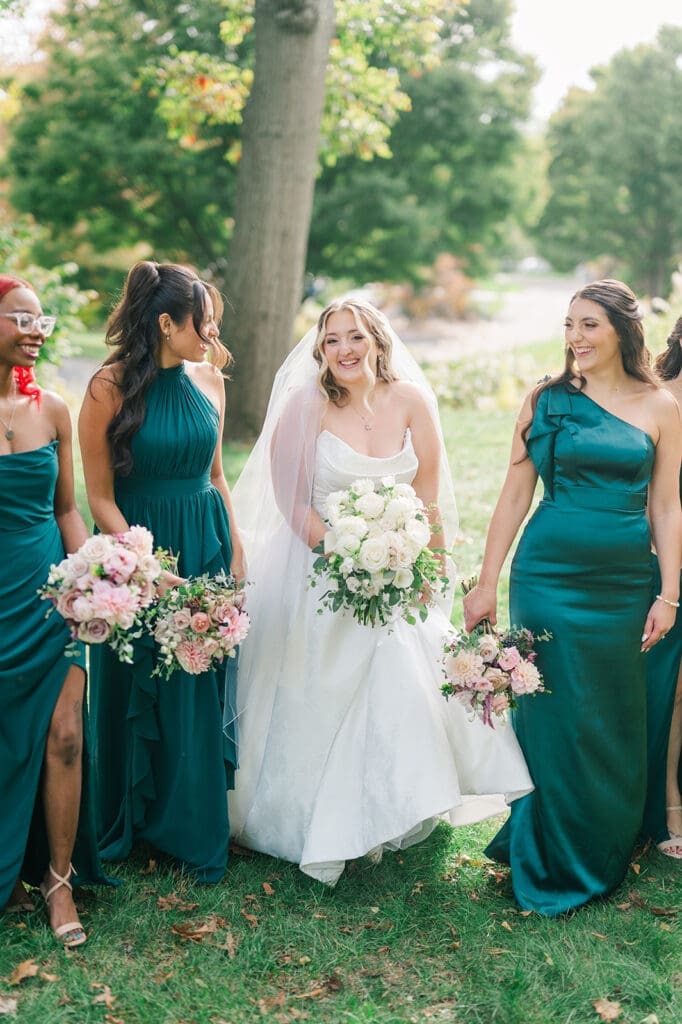 Magdalene and her bridesmaids hold their bouquets next to one another while walking and smiling. 
