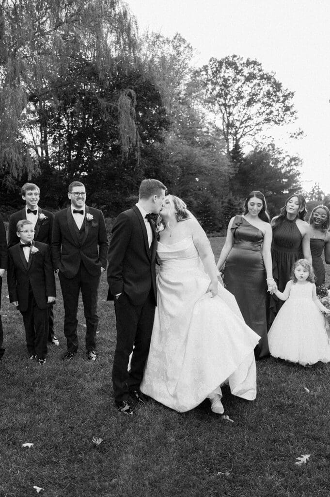 Magdalene and Trey kiss while their bridal party walks besides them on the lawn for their Woodwinds wedding