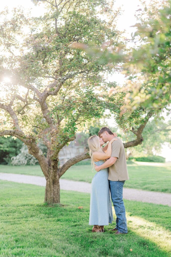 A woman kissing her fiance under a tree at Topsmead State Park for their engagement photos