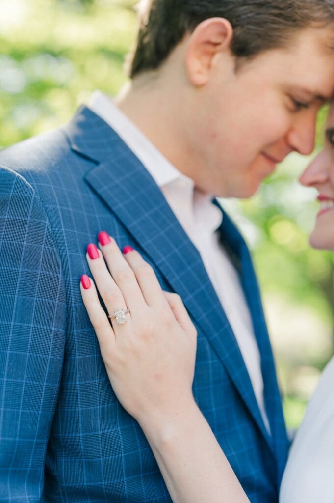 A hand with a radiant engagement ring resting on a suit jacket.