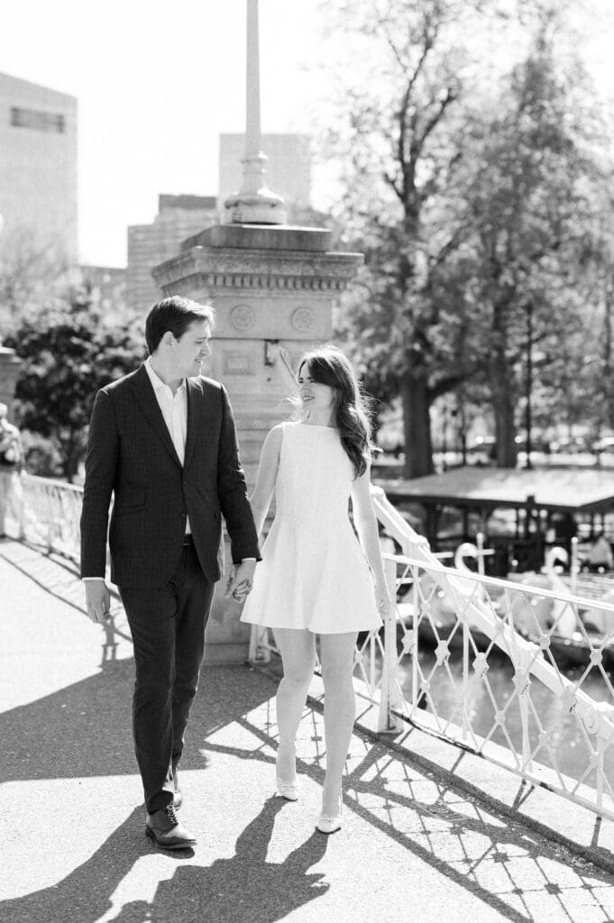 Julia and Brandon holding hands and walking on the bridge at the Boston Public Garden. 
