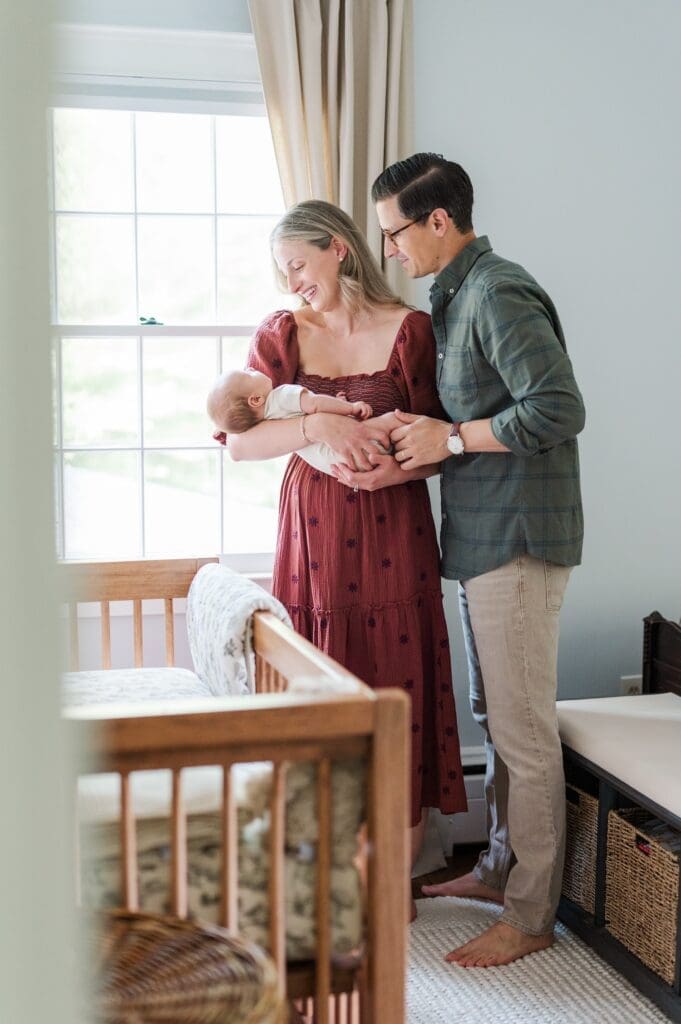 Baby G's mom and dad hold him by the windowsill and smile at him during their in-home newborn session. 