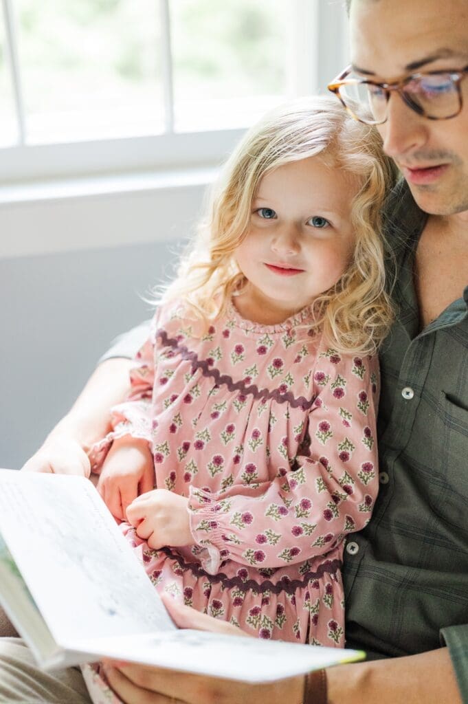Toddler sister smiles as dad reads to her