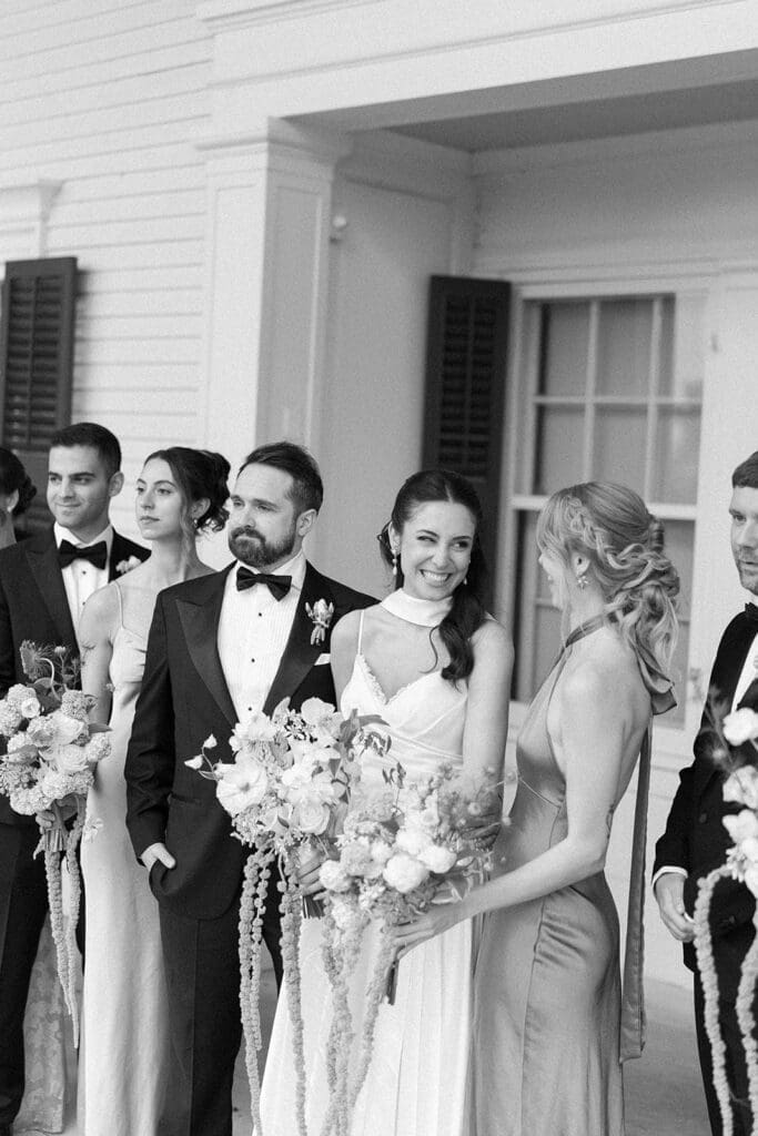 Natalie and Tom smile and laugh with their entire wedding party on the front porch. 