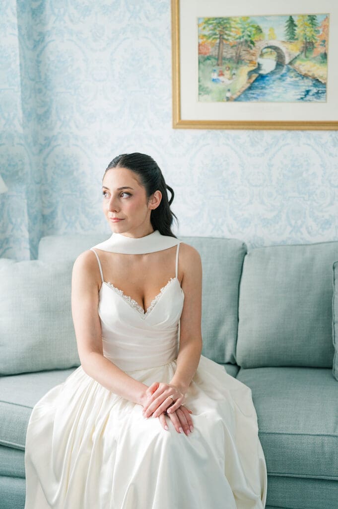 Natalie sits on a blue couch in her vintage wedding dress and scarf