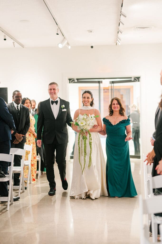 Natalie is walked down the wedding aisle by her mom and dad. 