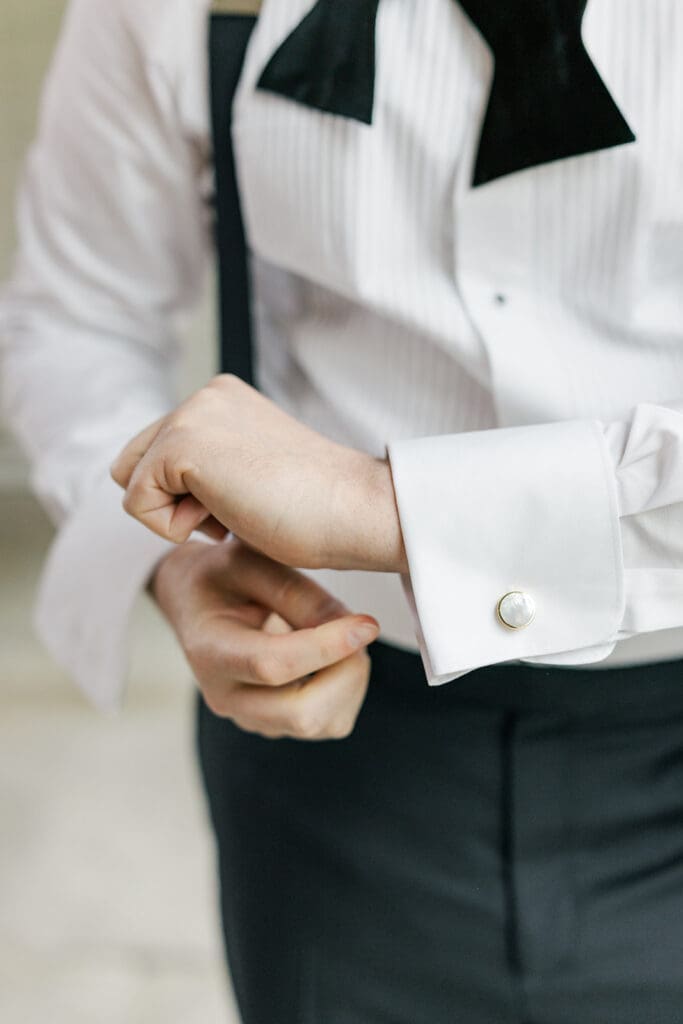 Tom adjusts the cufflinks on his shirt cuff. 
