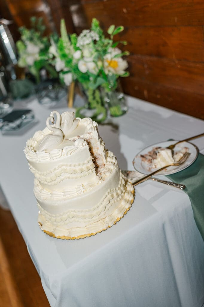 A vintage piping wedding cake with two swans on top. There is a piece missing from the cake. 