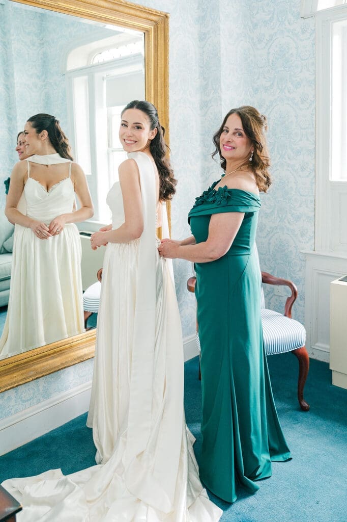 Natalie's mom buttons her up as they smile together. 
