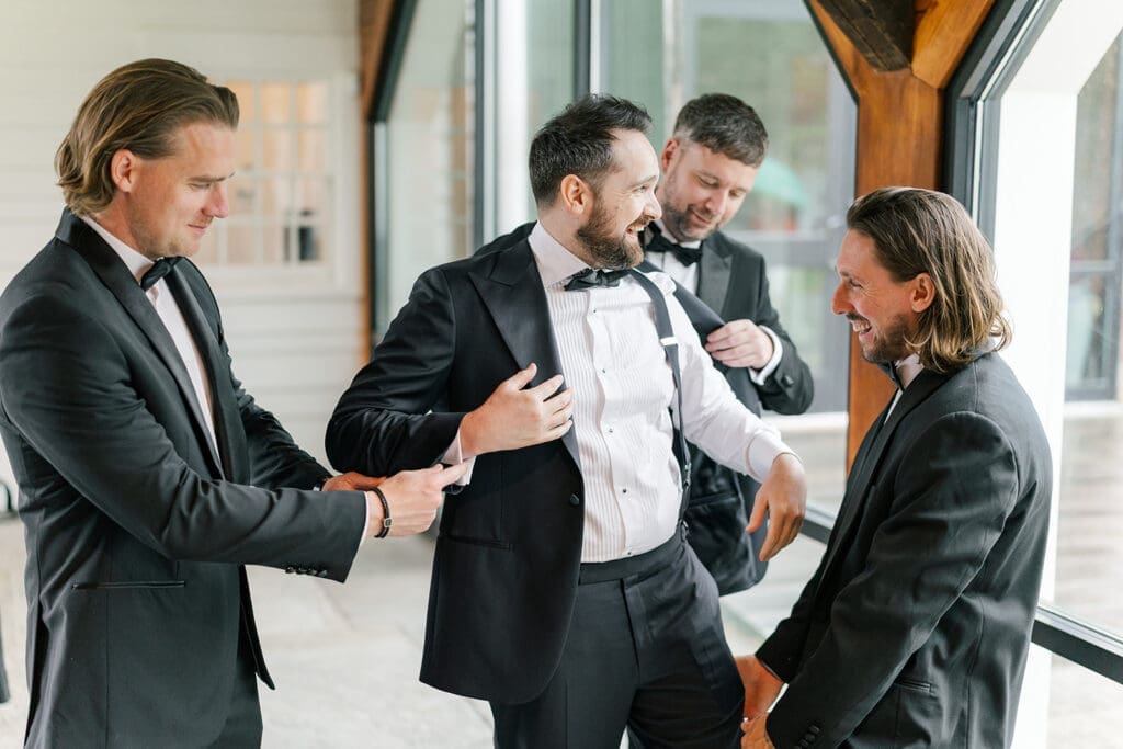 Groomsmen help tom put on his suite jacket. 