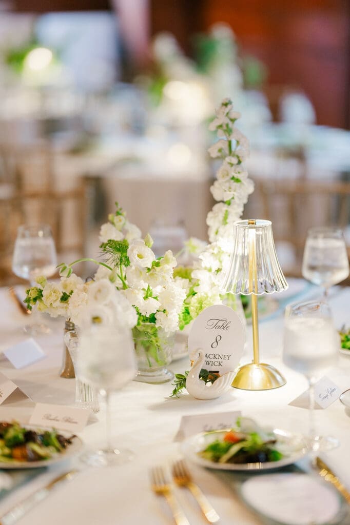 Table decor with menus, swan table numbers, table lamps, and salads. 