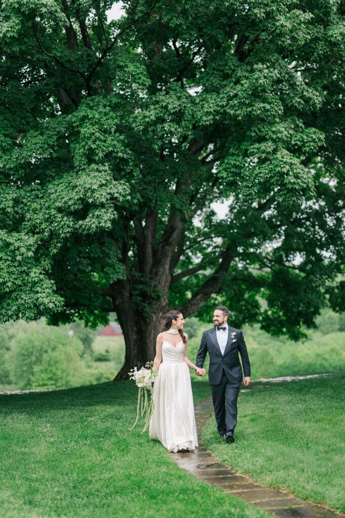 Natalie and Tom hold hands and walk outside Hill-Stead on their rainy wedding day. 