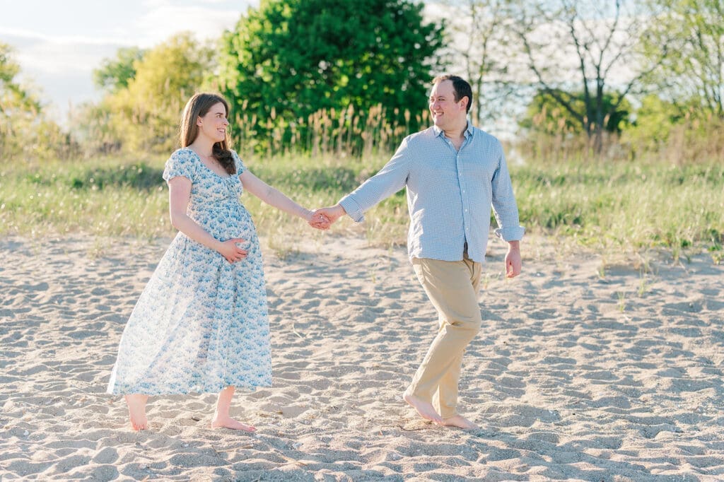 A man walks and leads his wife as she holds her belly. 