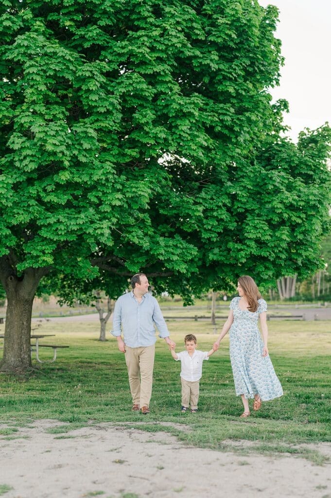 A family walks under a large tree at Sherwood Island State park as they smile together. 