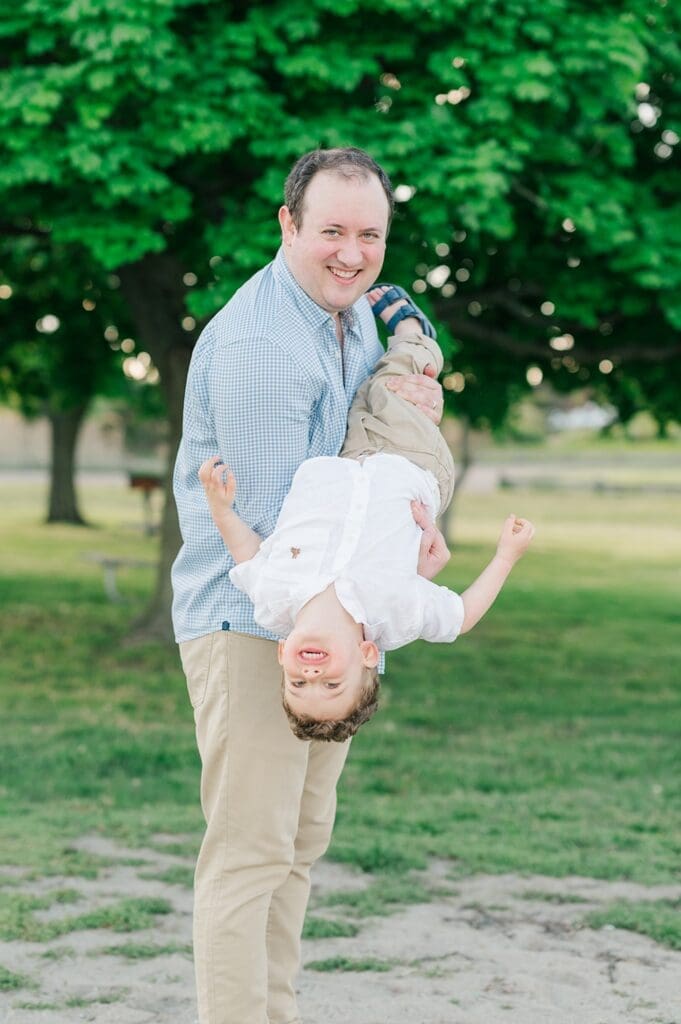 A man carries his son upside down and they both laugh. 