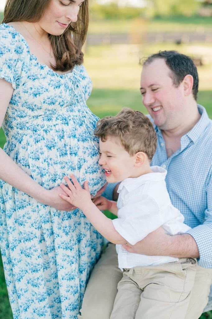 A toddler laughs as he hugs his mother's pregnant belly. 