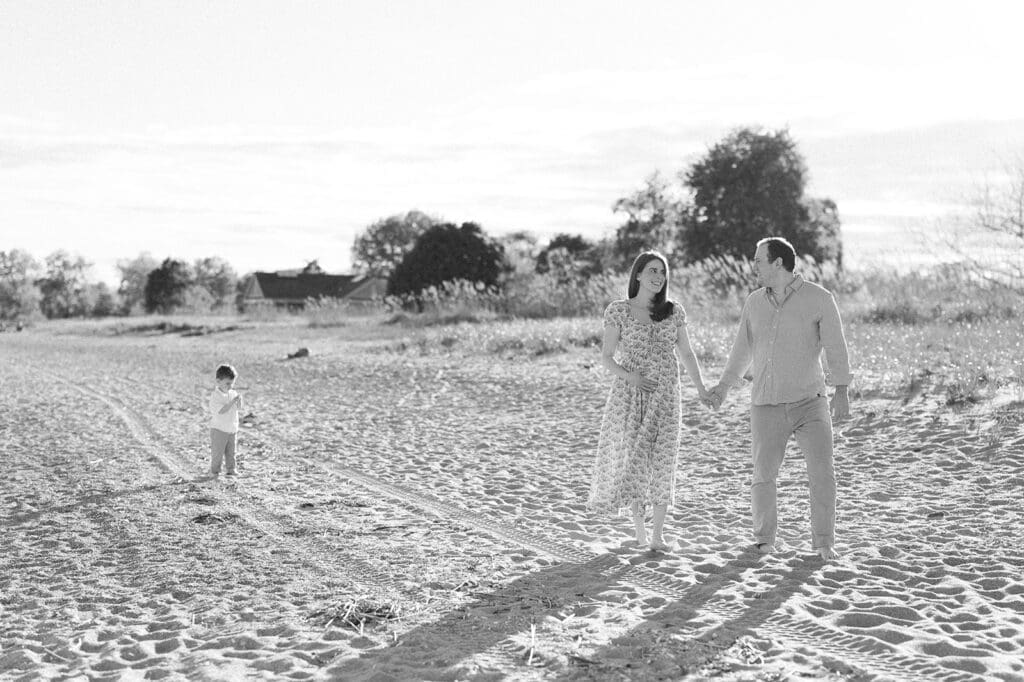 A man and woman walk on the sand at Sherwood Island State Park and their son follows behind. 