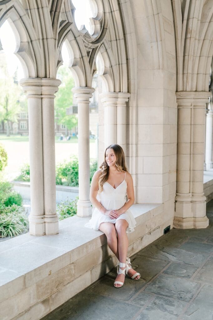 Sophia sits on a ledge near columns at Trinity college and smiles outdoors. 
