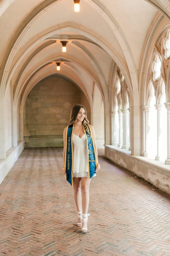 Sophia, a Trinity college grad, walking along a stone path under archways at the college chapel. 
