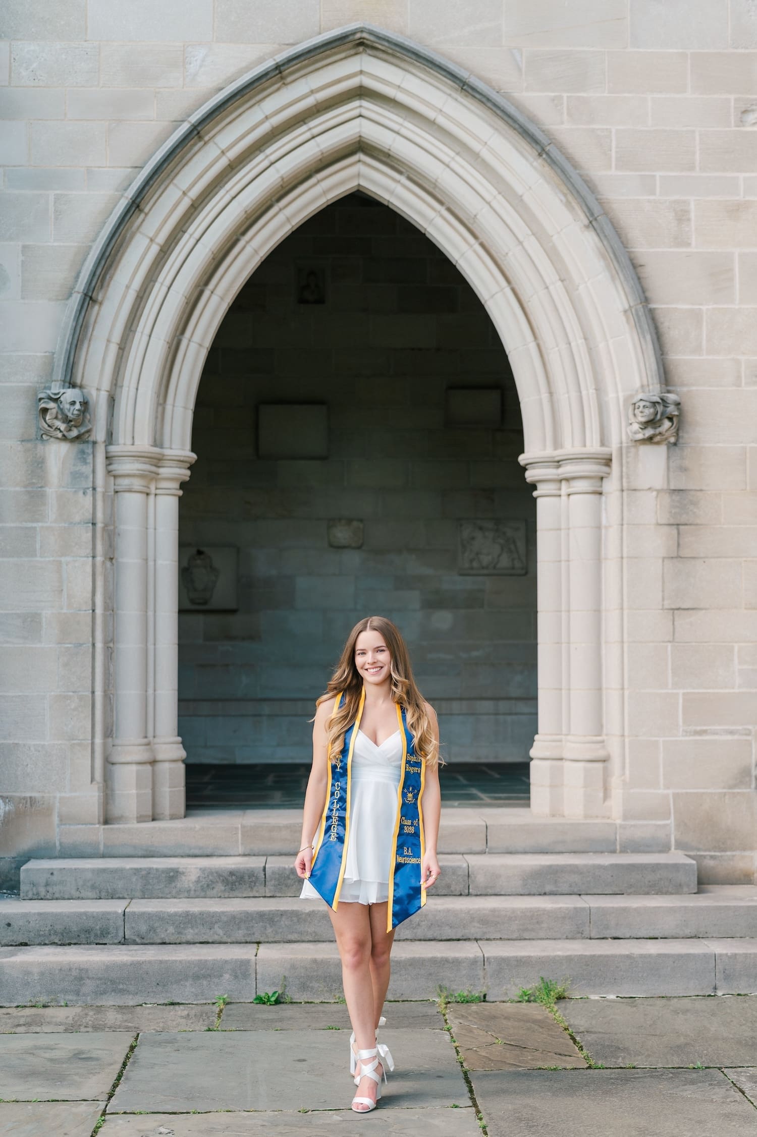 A Trinity College grad walking in front of an archway on campus