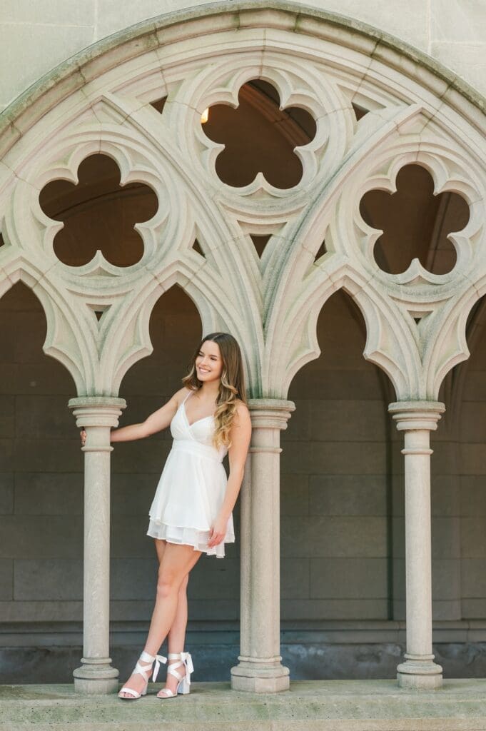 Sophia hangs off of a column smiling at the Trinity College chapel for her grad photos. 