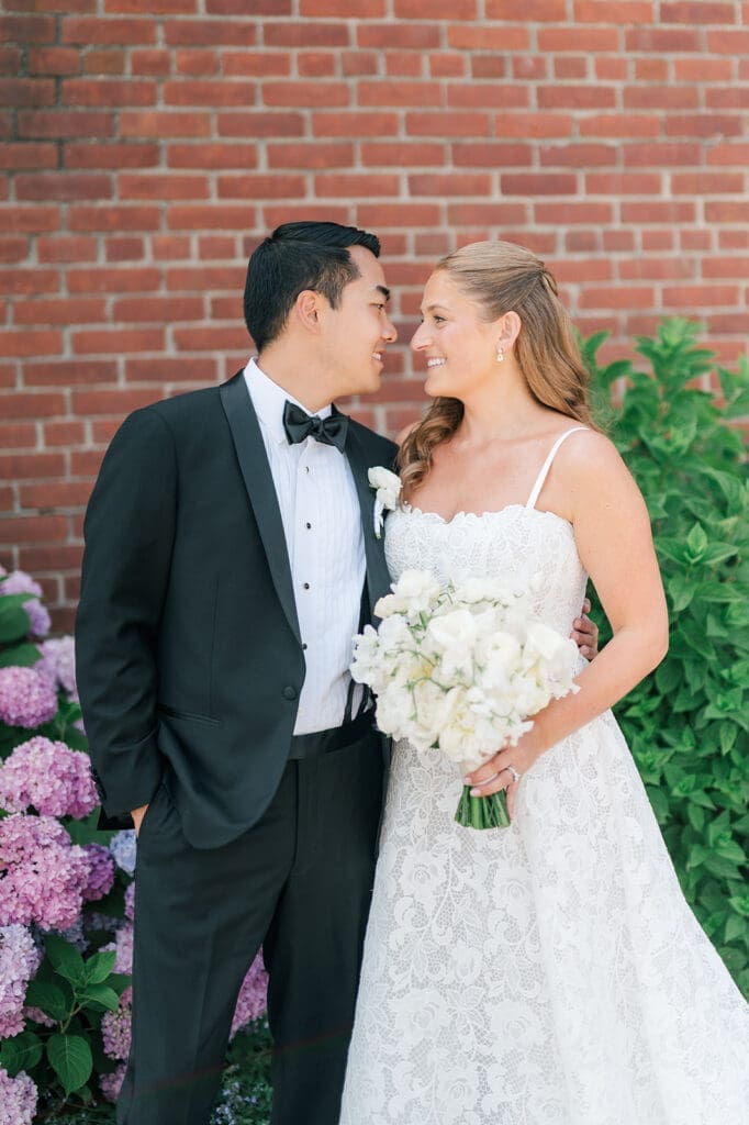 Katie and Sang nuzzle noses in front of pink and blue hydrangeas for their Delamar Greenwich wedding. 