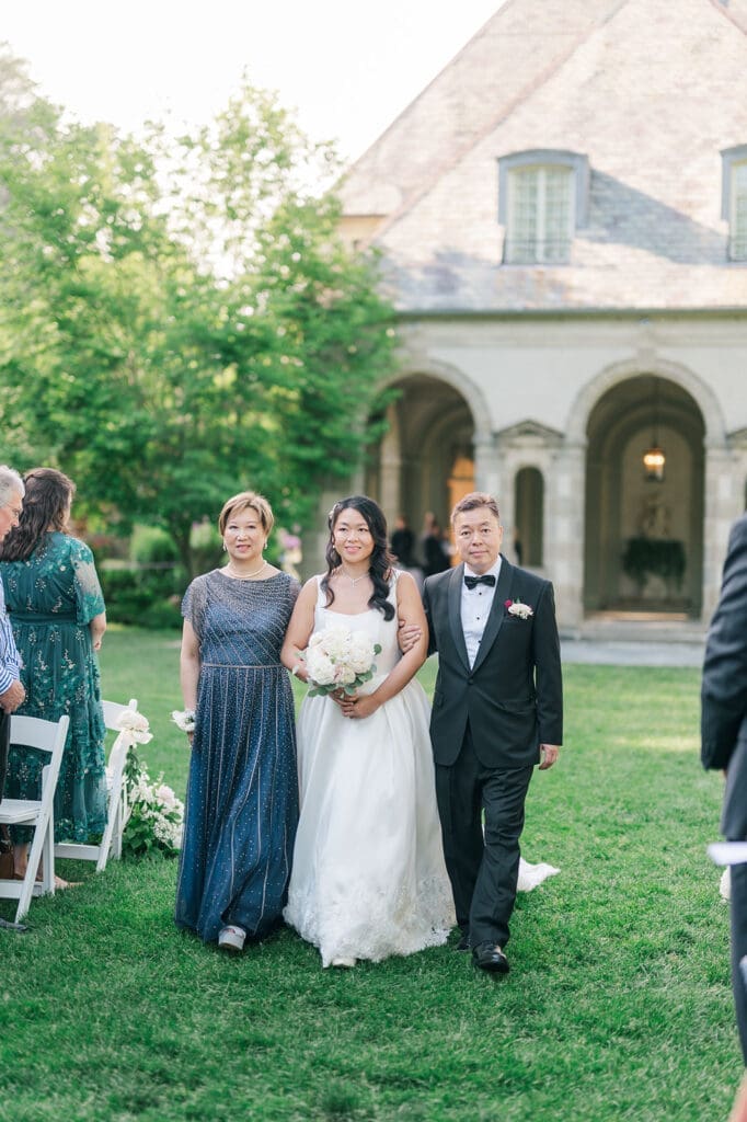Emily walks down the aisle, escorted by her parents