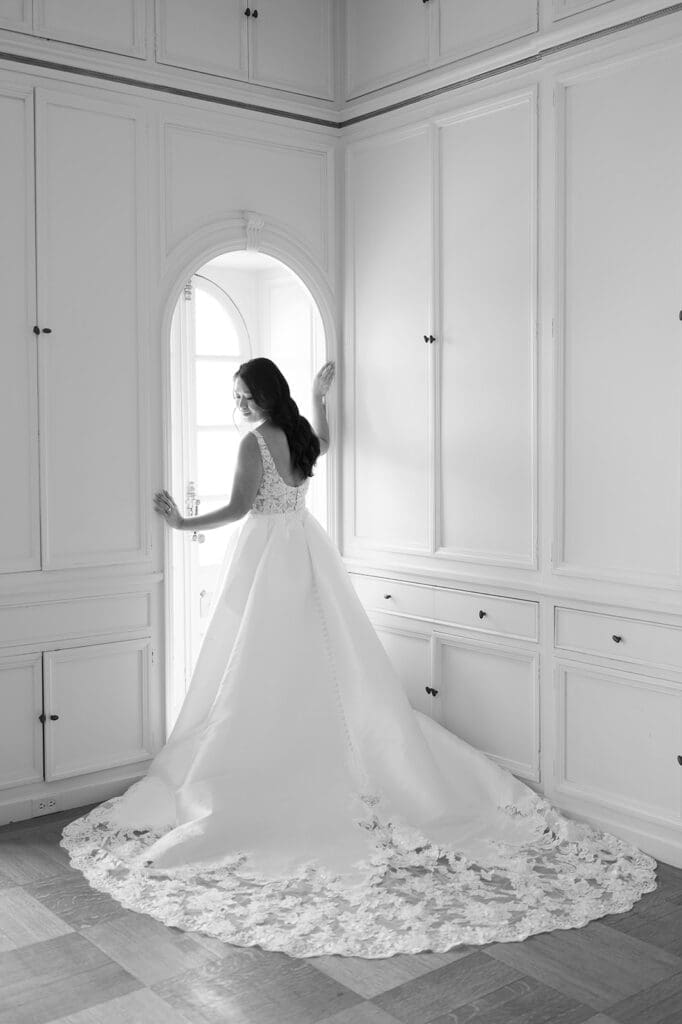 Emily peers over her shoulder and softly smiles as the window light peeks through the bridal suite