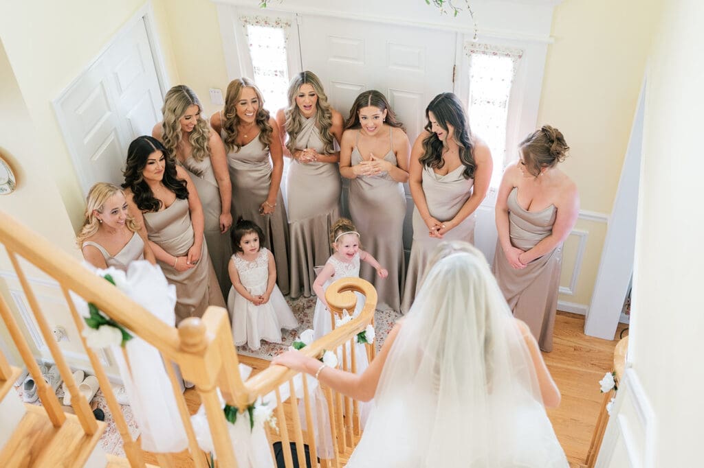 Jacquie does a first look with her bridesmaids as she walks down the stairs in her home. 