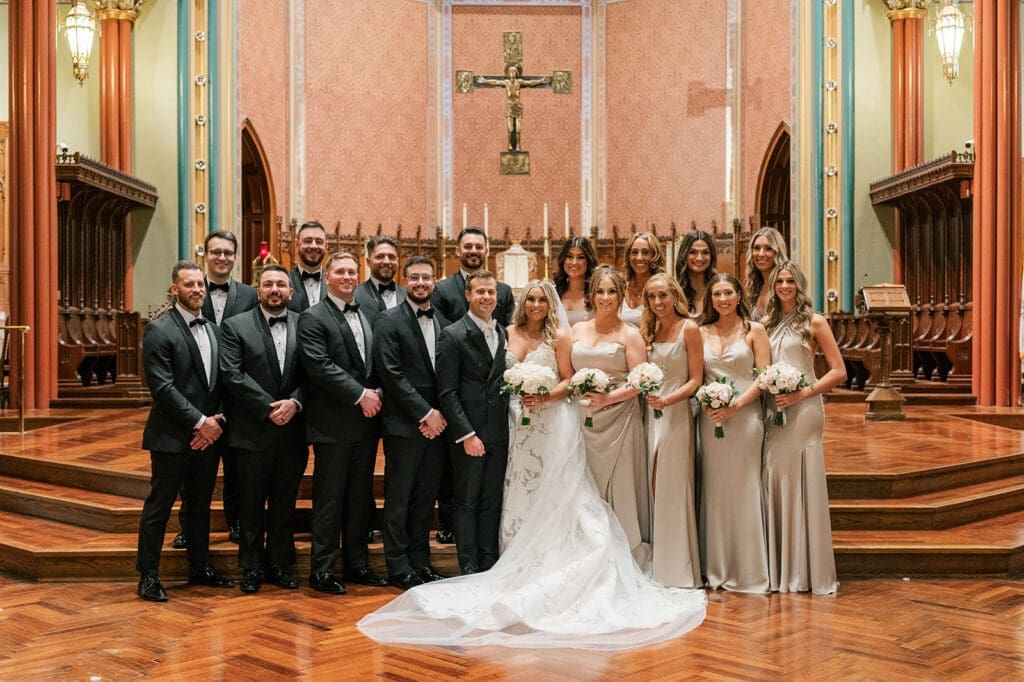 The full bridal party smiles and stands together in the church. 