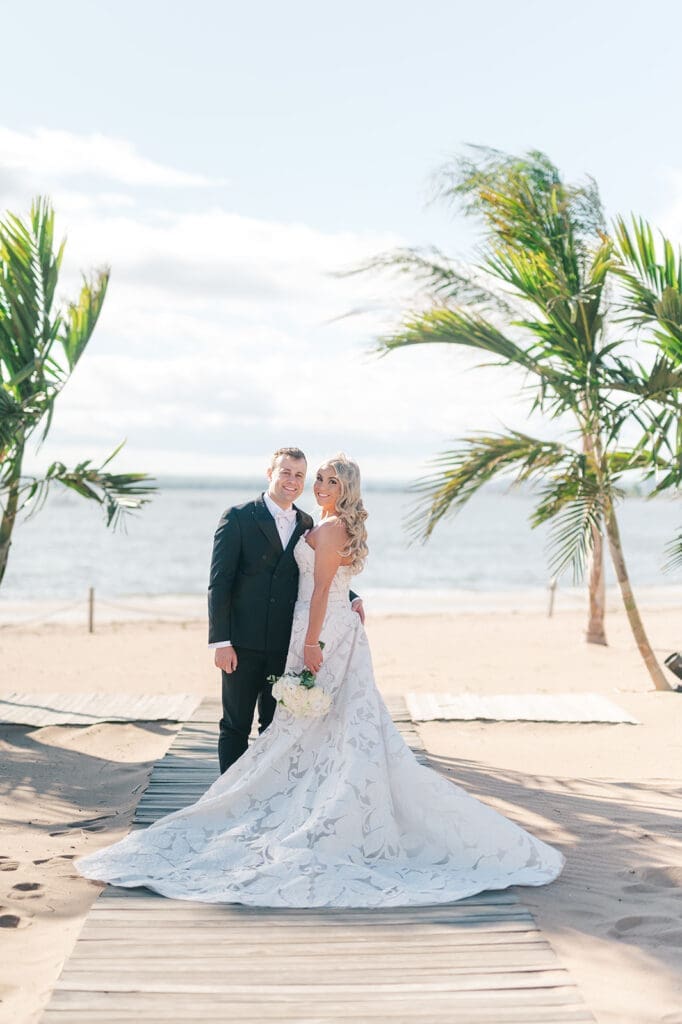 Jacquie an Thomas pose for a classic portrait under palm trees at  their Anthony's Ocean View wedding. 