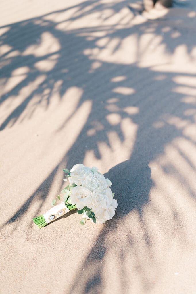 Jacquie's bridal bouquet lays on the sand in the shadows of palm trees. 