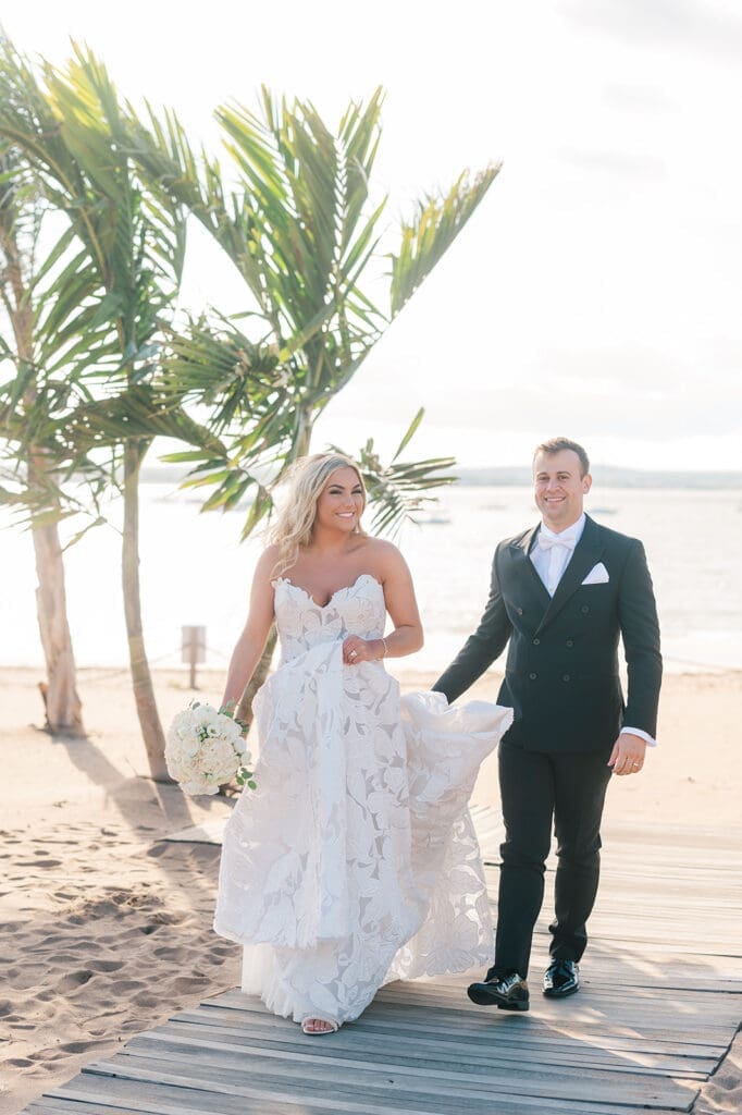 Jacquie an Thomas walk under palm trees at their Anthony's Ocean View wedding. 