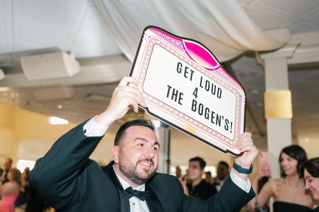 A groomsman holds a sign that says "Get loud 4 the Bogens"