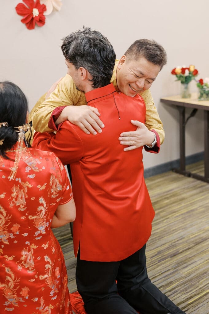 The bride's dad hugs the groom smiling. 