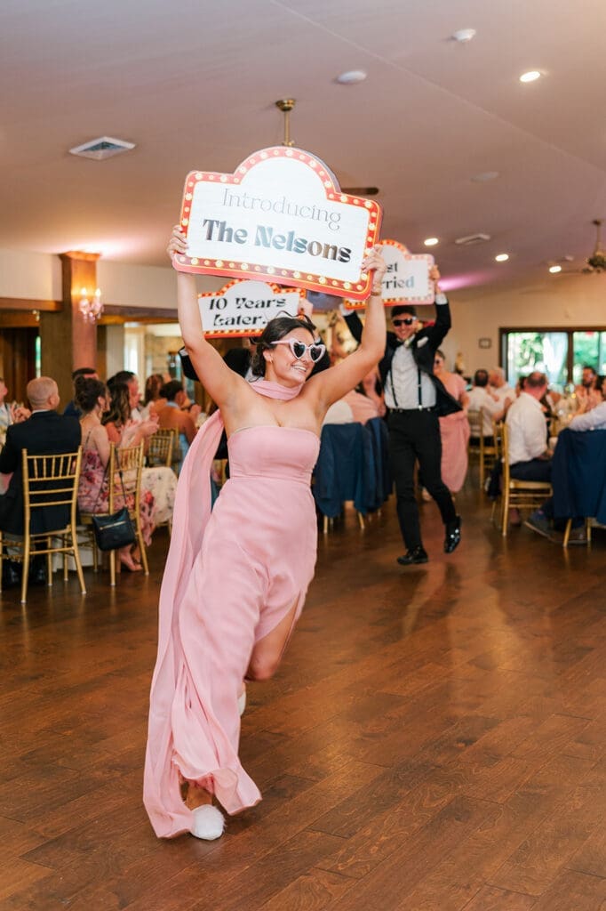 the wedding party runs out with signs that say "Introducing the Nelsons" and "10 years later..." during the wedding reception