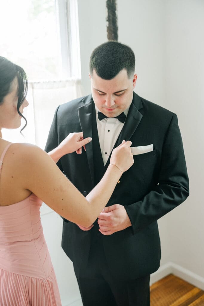 A bridesmaid adjusting John's jacket